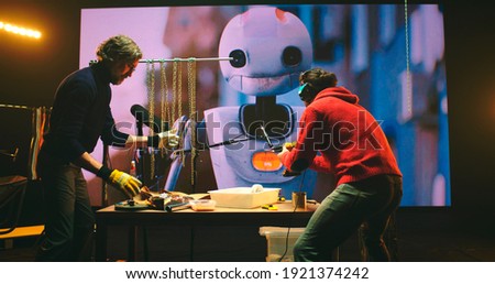 View of male sound designers recording clinking of chains and drill buzz while creating audio for 3D cartoon about robot