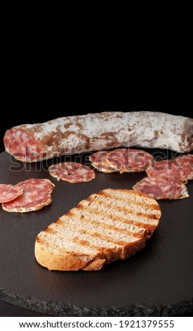
The sausage is cut into pieces, lying on a black board photographed in macro photography. With a piece of toasted bread.