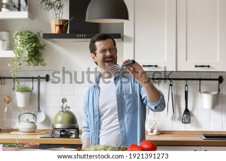 Excited funny millennial Caucasian man enjoy cooking healthy food sign in kitchen appliances in modern home. Happy young male have fun preparing delicious dinner or breakfast in the morning.