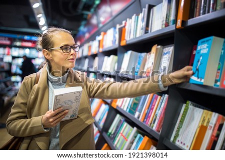 Pretty, young female choosing a good book to buy in a bookstore Royalty-Free Stock Photo #1921398014