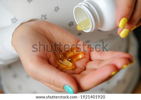 Woman hand holds yellow medication capsules of omega 3. Pregnant girl accepts the fish oil.