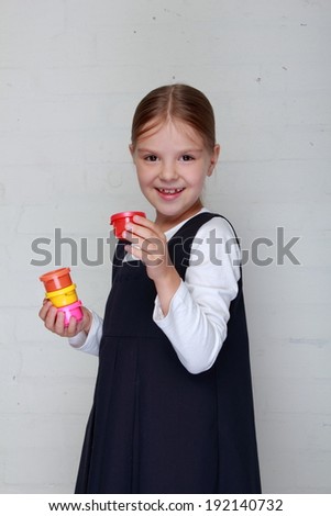 Cute little schoolgirl in the form of holding the paint for drawing on a gray background