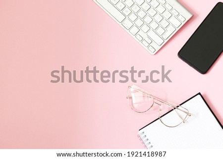 pink background with spiral notebook, mobile phone, glasses and keyboard