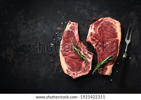 Two raw dry aged beef rib steaks (cote de boeuf)  with rosemary, pepper and salt on dark background Royalty-Free Stock Photo #1921422311
