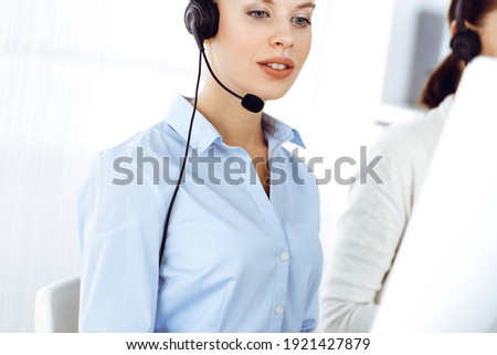 Blond woman call operator is using computer and headset for consulting clients online. Group of diverse people working as customer service occupation. Business concept