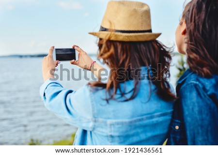 Young women outdoors taking photo with smartphone standing together. 