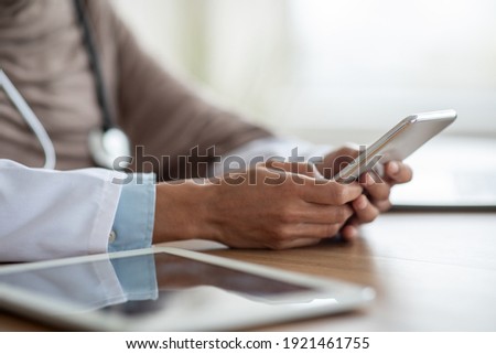 Cropped of female doctor using gadgets at workplace, holding smartphone and digital tablet. Unrecognizable therapist having online conversation with her patients, using mobile phone, closeup Royalty-Free Stock Photo #1921461755