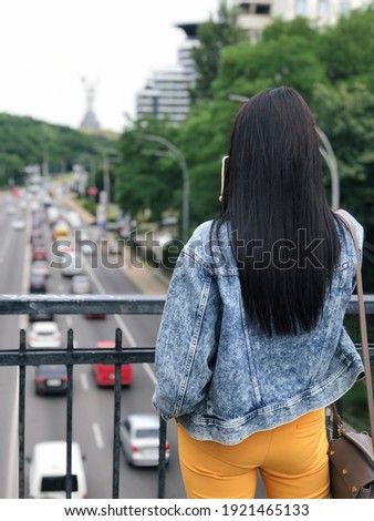 The girl stands on the bridge and takes pictures of the city view. Kyiv. Kiev. Ukraine. Brunette. Street fashion