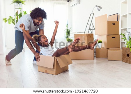 Father push cute little daughter sitting inside of carton box having fun riding in living room. Loan mortgage, housing improvement concept. Cheerful happy african family enjoy relocation day. Royalty-Free Stock Photo #1921469720