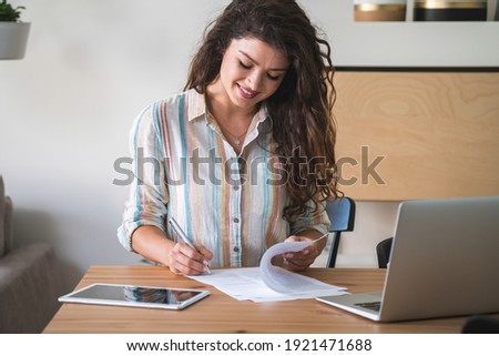Business contract signing. Businesswoman signs formal paper with pen on table with laptop computer and digital tablet. Smiling woman doing paper work at home