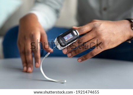Unrecognizable African Man Using Pulse-Oximeter Checking Oxygen Saturation And Pulse Rate Sitting At Home. Pulseoxymetry Medical Device On Male Hand Measuring Ox Level. Cropped, Selective Focus Royalty-Free Stock Photo #1921474655