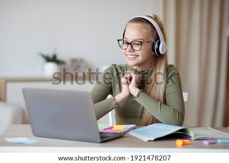 E-education, online lessons and courses for schoolers. Joyful teen blonde girl in headset looking at laptop screen, watching online lesson or listening to tutor, home interior, copy space
