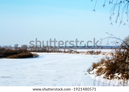 
Beautiful calm winter landscape.
A frozen river with trees along the coastline. Snowy coastline of the river. Frosty winter day. Blue tinted.