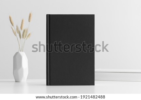 Black book mockup with a lagurus and workspace accessories on a white table.
