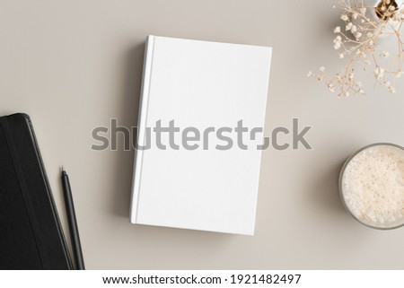 White book mockup with a gypsophila, coffee and workspace accessories on a beige table. Royalty-Free Stock Photo #1921482497