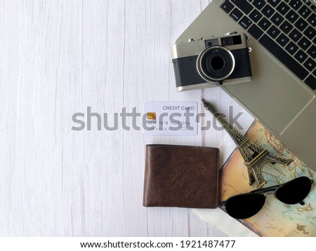 Top view of accessories for travelers to travel in a great journey. Camera with brown wallet with credit card and sun glasses on the map on white wooden background and laptop on Traveling concept.