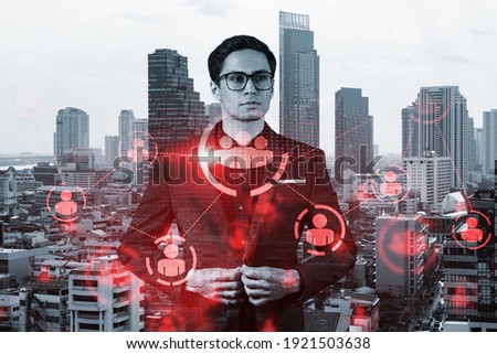 Handsome eastern HR director at international company is thinking about efficient strategy to recruit highly qualified specialists. Social media and marketing hologram icons over Bangkok background.
