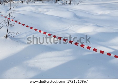 Red and white striped warning tape on a snow background. Limited access to the park during the coronavirus pandemic. Quarantine zone