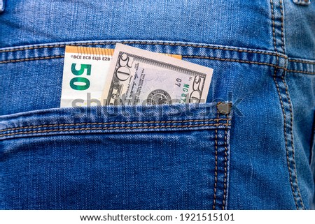 Banknotes in denominations of 50 euros and dollars in blue jeans back pocket close-up.
