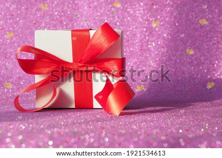 gift box with a red bow on a purple glittering background. bokeh multicolored hearts. copy space.
