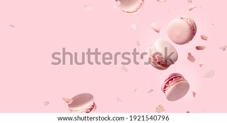 French macarons flying in the air among the crumbs on pink background. Levitation concept. Food wide banner with copyspace. Royalty-Free Stock Photo #1921540796