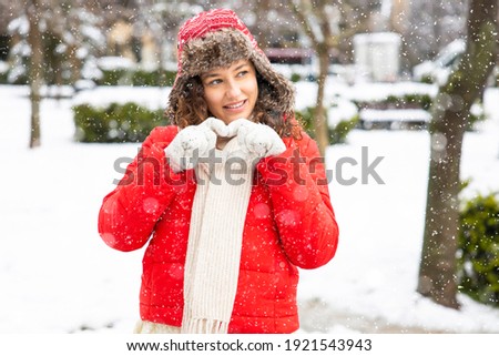 Young smiling woman make heart shape with hands in winter gloves. Snowy winter season in the city