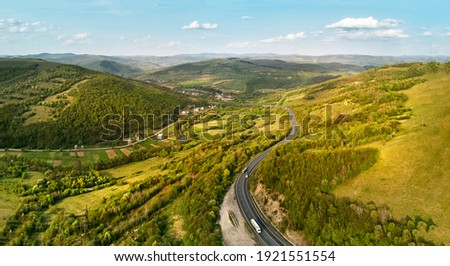 Highway in mountains. Evening sunlight on hills. Spring green rural landscape. Aerial view on road in hills with sunset light. Beskid range of Carpathian mountains, Ukraine