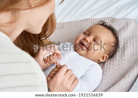 Caucasian mum, foster single parent holding hands of happy cute adorable adopted infant african american baby girl daughter lying on bed. Child care, diverse ethnicity mother and child concept. Royalty-Free Stock Photo #1921556639