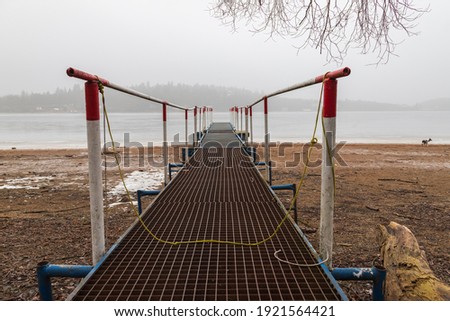 Metal pier leading to the frozen surface of the drained dam. There is fog in the background.