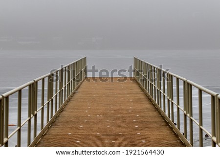 Metal pier leading to the surface of the drained dam. There is fog in the background.