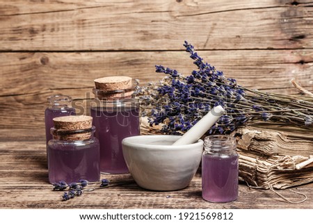 Dried lavender flowers in a in a mortar and pestle with bottle of essential lavender oil or infused water. Old books and lavender flowers bunch in the wooden background, place for text Royalty-Free Stock Photo #1921569812