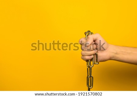 Male hand holding a metal chain on a yellow background indoors. Copy space.
