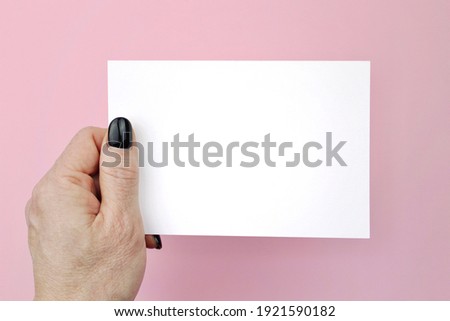 Creative flat lay top view of woman hands black manicure with paper page on pink background