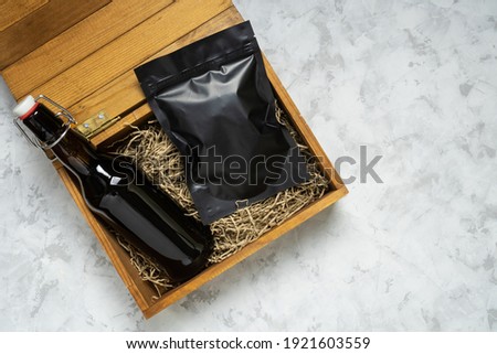 Bottle of craft beer and packaging of snacks in a wooden gift box on grey concrete background with copy space. Royalty-Free Stock Photo #1921603559