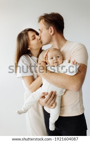 Romantic portrait of a young family, kissing, showing their feelings to each other. A young dad is holding a little daughter in his arms, which is cute posing for the camera. High quality photo