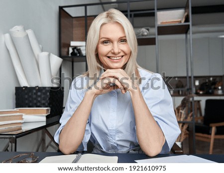 Smiling mid aged business woman looking at web cam video conference calling in virtual chat meeting, giving remote training webinar class working from home office. Headshot face portrait. Webcam view Royalty-Free Stock Photo #1921610975