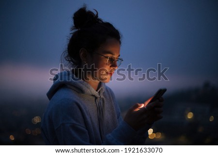 Beautiful young woman use smartphone at night. Millennial generation z female scroll through news feed on app on her phone. Cinematic film look photo of pretty woman at sunset use phone Royalty-Free Stock Photo #1921633070