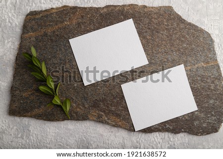 White paper business card, mockup with natural stone and boxwood branch on gray concrete background. Blank, flat lay, top view, still life, copy space.