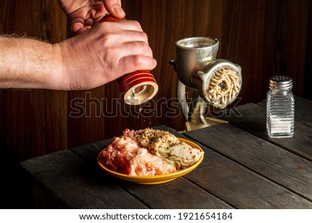 Cooking cutlets with the hands of a chef on a dark background. Add pepper to the minced meat. Free space for restaurant advertising lettering