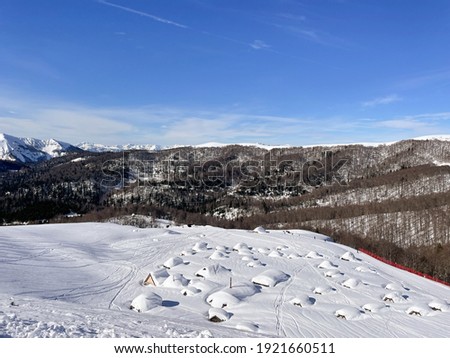 Houses under the snow in the mountains against the background of mountains and a bright blue sky. North of Montenegro there is a lot of snow, no one is at home 