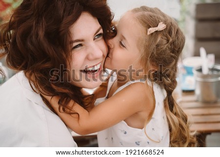 Portrait of little daughter kissing her beautiful happy mother