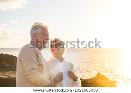 close up and portrait of two happy and active seniors or pensioners having fun and enjoying looking at the sunset smiling with the sea - old people outdoors enjoying vacations together Royalty-Free Stock Photo #1921685030
