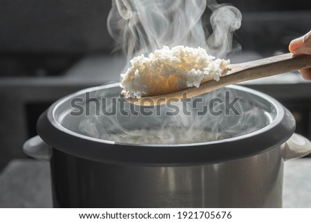 The steam from  Hand hold wooden ladle in electric rice cooker in the kitchen.hot food concept Royalty-Free Stock Photo #1921705676
