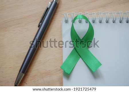 Mental Health conceptual. Green ribbon on open notebook. Wooden background.