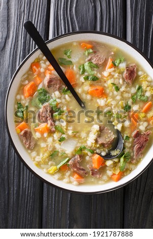 Scotch broth is a traditional Scottish soup made from lamb, and vegetables, barley, peas closeup in the plate on the table. Vertical top view from above
