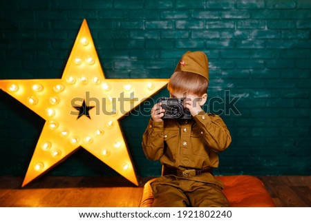 Beautiful smiling boy holding a camera. Young photographer. Child taking photos in professional photo studio. Happy child photographer with film camera. Cute kid takes picture with vintage camera