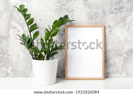 Wooden vertical frame with white blank card, and green houseplant flower in pot on table on gray concrete wall background. Mockup Template for your design, text.