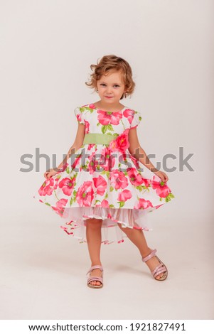 Сute 4-5 year old girl in style dress on white isolated background looks at camera. Concept Birthday and Children Celebration. Little child in colorful sundress posing and showing emotions. Copy space