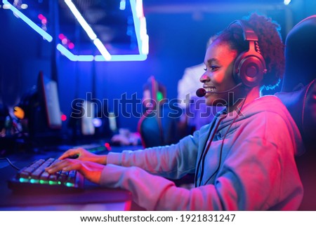 Streamer african young woman rejoices in victory professional gamer playing online games computer with headphones, neon color.