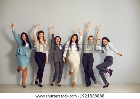 Success, business development, woman office workers staff. Smiling positive women workers jumping and celebrating business win in corporate project with hands raised over grey wall background Royalty-Free Stock Photo #1921838888